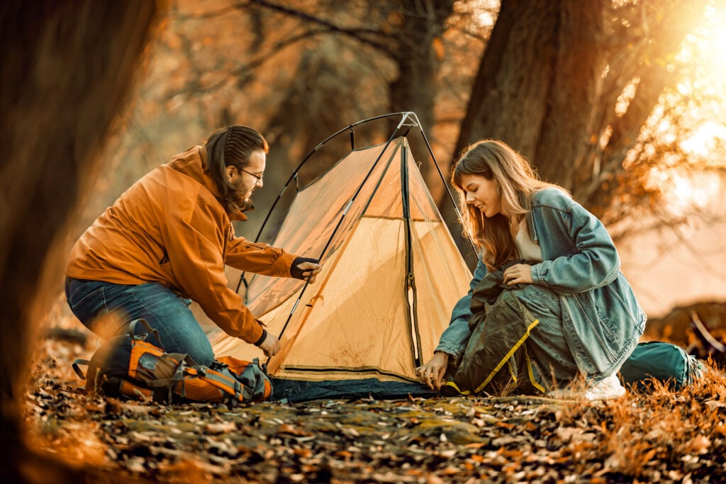 Couple sets up tent in autumn forest.