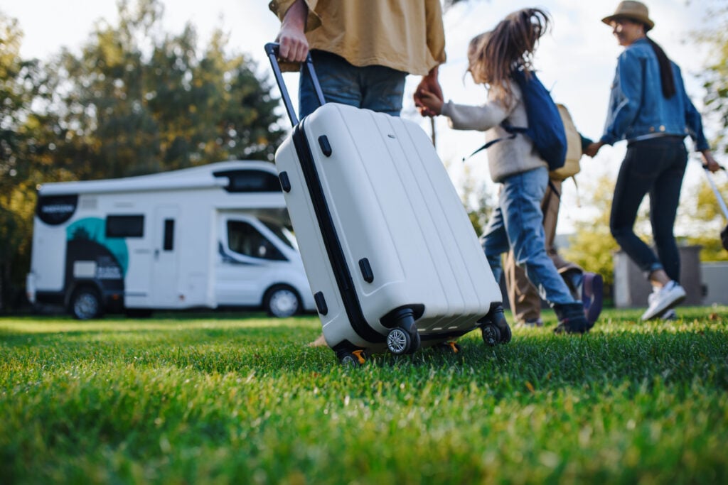 Family with luggage near RV on green grass.
