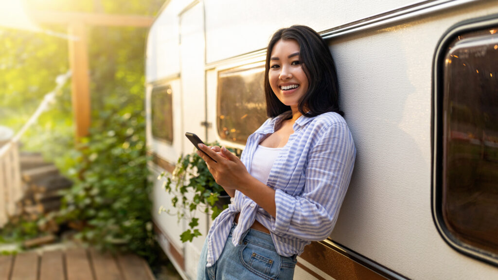 Smiling woman using smartphone near camper outdoors