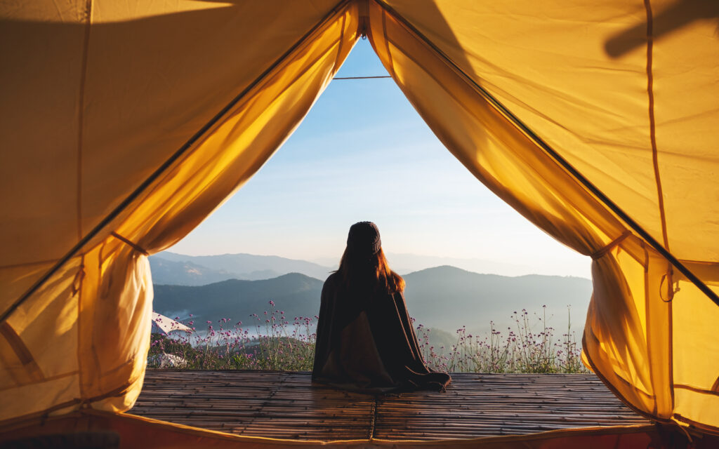 Person sitting in tent, overlooking scenic mountains.