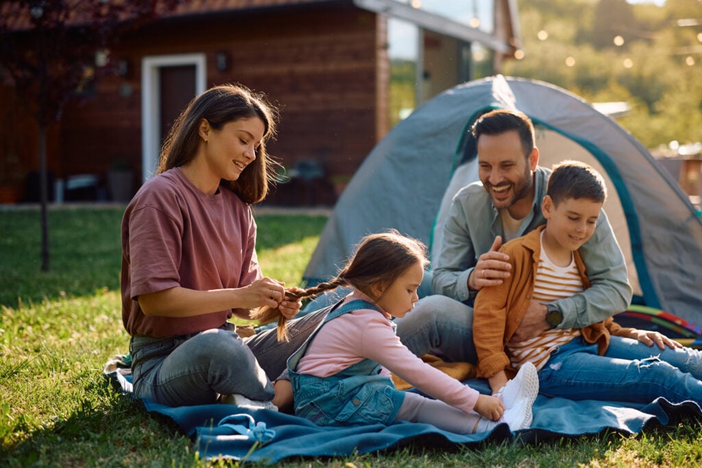 Family camping, woman braiding girl's hair outdoors.