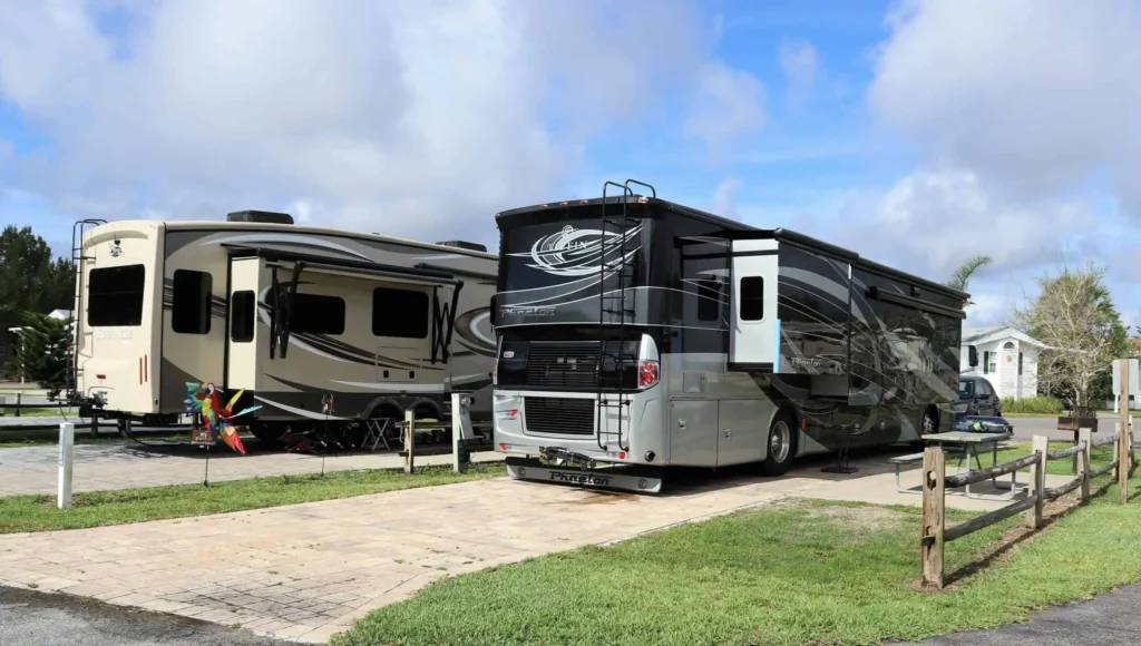 Two RVs parked at a campsite under cloudy sky.